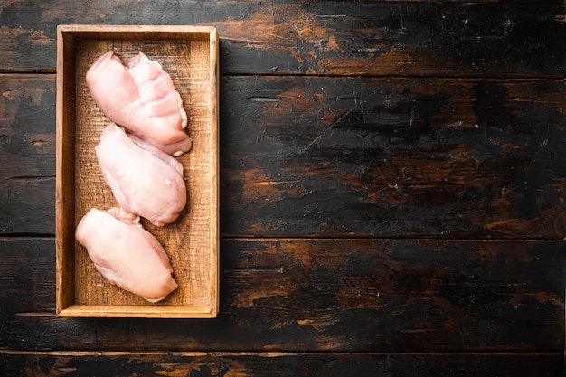 Filetes de pechuga de pollo, en caja de madera, sobre la vieja mesa de madera oscura.