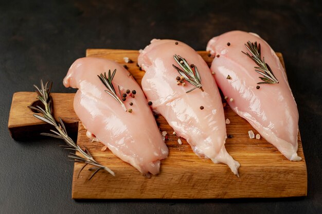 Filetes de pechuga de pollo cruda, listos para cocinar en una tabla de cortar de madera con especias.