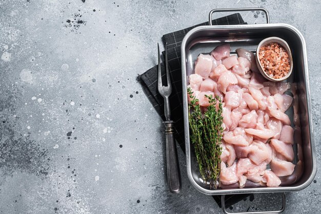 Filetes de pechuga de pollo crudo cortado en cubitos en bandeja de acero Fondo gris Vista superior Espacio de copia