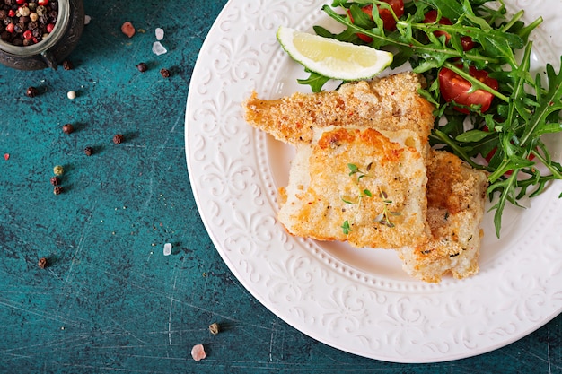 Filetes de pescado blanco frito y ensalada de tomate con rúcula. Vista superior