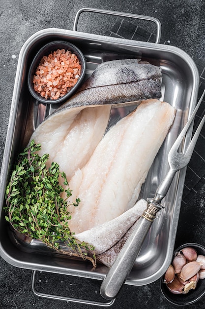 Filetes de pescado de eglefino crudo carne de pescado blanco en bandeja de cocina con tomillo Fondo negro Vista superior