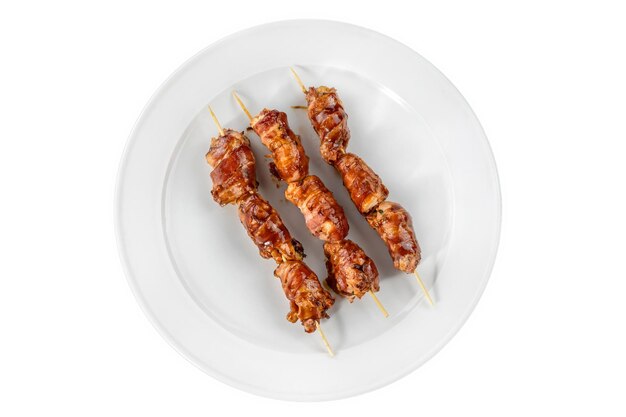 Los filetes de pollo envueltos en tocino a la parrilla se colocan en un plato blanco Ensartados en brochetas de madera Vista superior