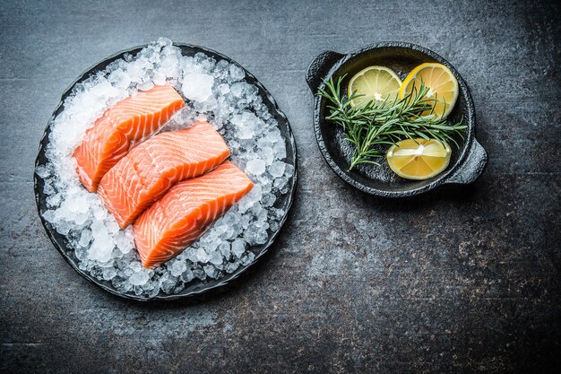 Filetes de salmón crudo en porciones en hielo en plato con limón y romero.