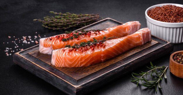 Filetes de salmón fresco en tabla de cortar negra con hierbas y especias