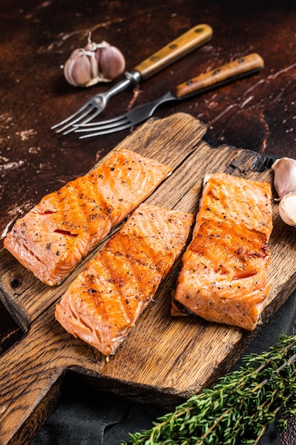 Filetes de salmón a la parrilla, filetes de pescado sobre tabla de madera con tomillo. fondo oscuro Vista superior.