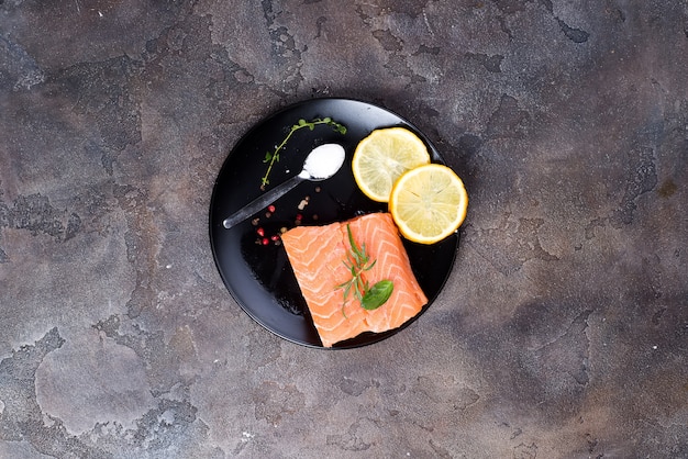 Filetes de salmón sobre hielo con limón y sal en un plato negro. Proteínas magras.