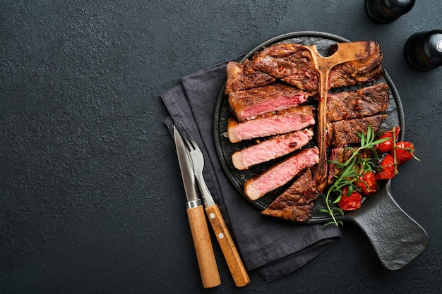 Filetes Tbone Rodajas de ternera a la parrilla Tbone o bistec de carne con especias romero y pimienta en tablero de mármol negro sobre fondo de madera vieja Vista superior Maqueta