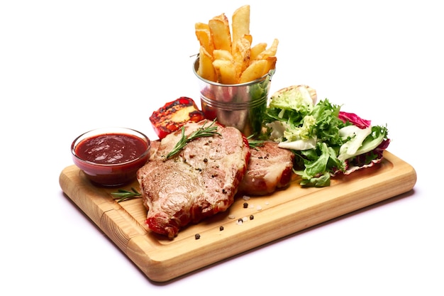 Filetes de ternera asada a la parrilla con salsa de patata y ensalada en la tabla de cortar de madera