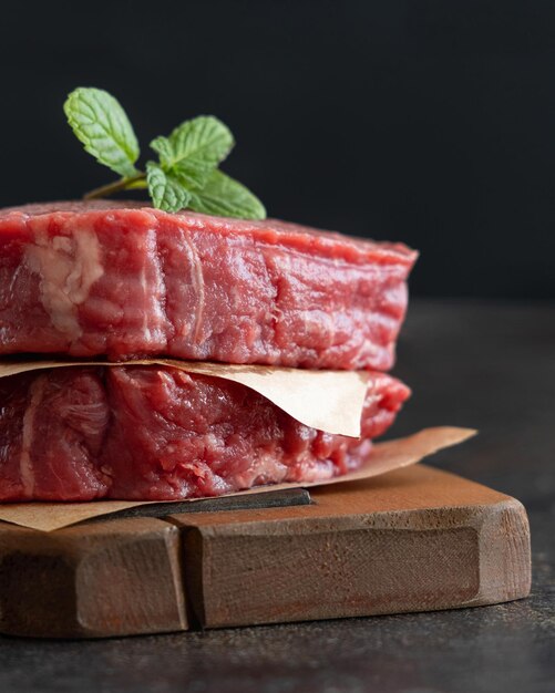 Filetes de ternera cruda sobre tabla de madera sobre fondo oscuro de cerca Filet mignons en porciones con especias e ingredientes Concepto de comida de verano