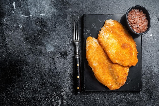 Filetes de tilapia empanados fritos sobre una placa de mármol Fondo negro Vista superior Espacio de copia