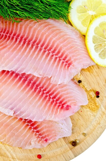 Filetes de tilapia con eneldo, limón y pimienta en una tabla de madera aislada sobre un fondo blanco