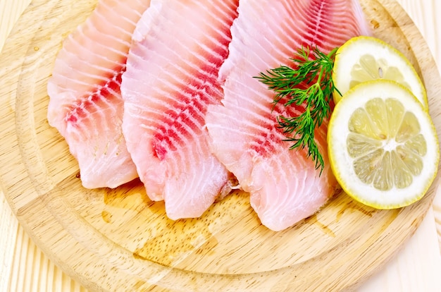 Filetes de tilapia con una ramita de eneldo, limón contra una tabla de madera