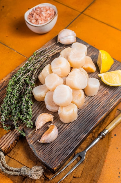 Filetes de vieiras crudas sin cocer sobre una tabla de madera con tomillo y limón Fondo naranja Vista superior