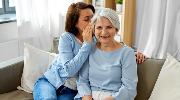 Foto filha adulta a sussurrar à mãe mais velha em casa.