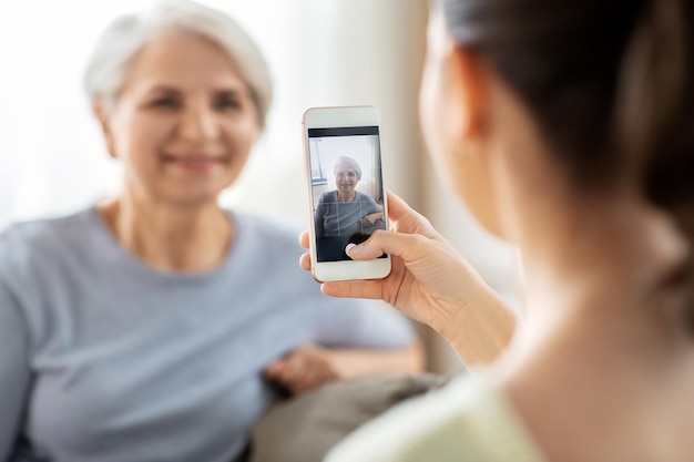filha adulta fotografando mãe idosa em casa