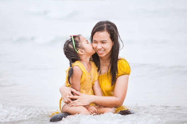 Filha asiática bonito beijar sua mãe com amor na praia em férias de verão
