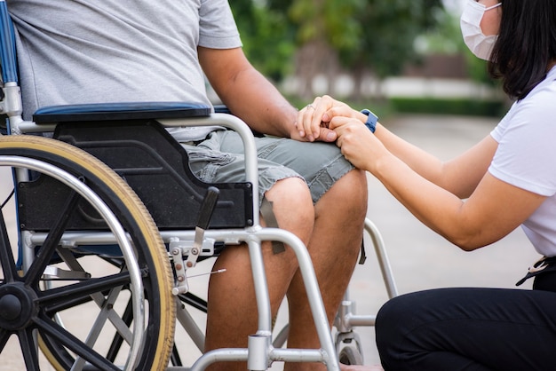 Filha asiática conversando e confortando pai em cadeira de rodas
