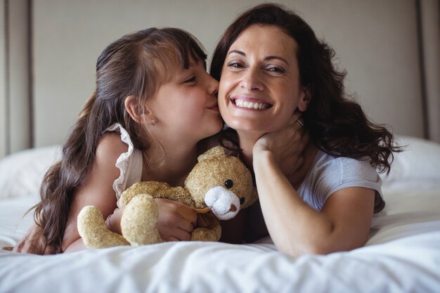 Filha beijando sua mãe na bochecha no quarto