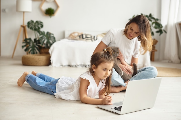 Filha brinca com a mãe e o gato enquanto a mãe trabalha no computador