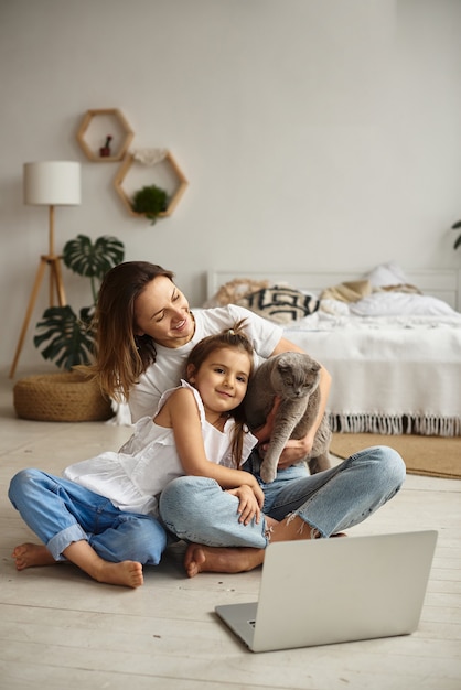 Filha brinca com a mãe e o gato enquanto a mãe trabalha no computador