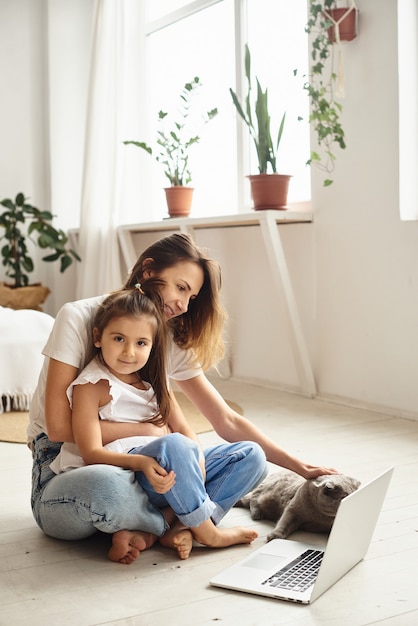 Filha brinca com a mãe e o gato enquanto a mãe trabalha no computador