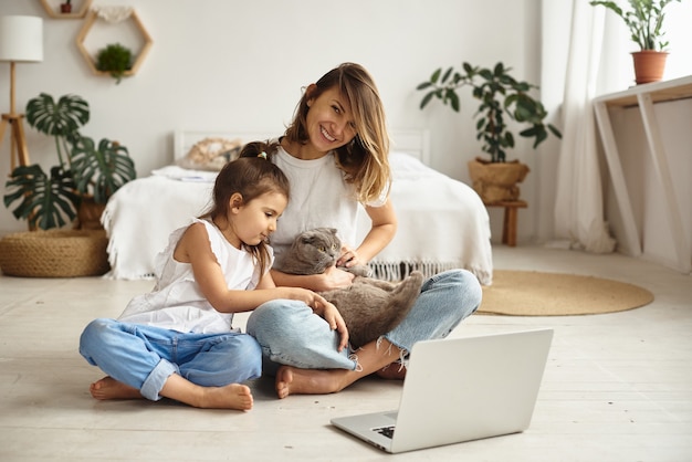 Filha brinca com a mãe e o gato enquanto a mãe trabalha no computador