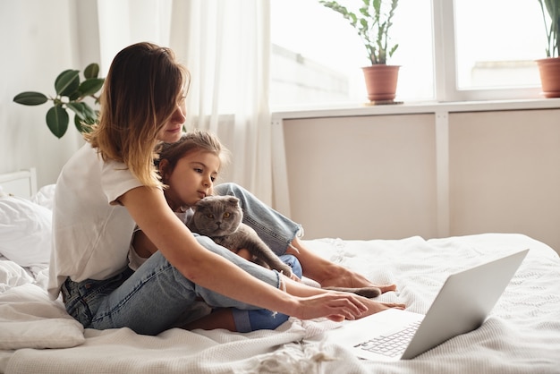 Filha brinca com a mãe e o gato enquanto a mãe trabalha no computador