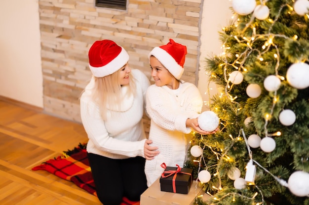 Filha com a mãe perto da árvore de Natal.