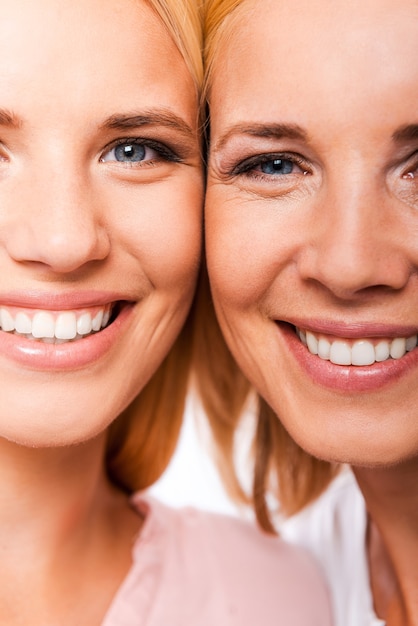 Filha com mãe. close-up de mãe e filha sorrindo e olhando para a câmera em pé, face a face, contra um fundo branco