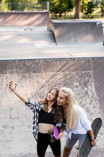 Filha de mãe e filho com skate e penny board está fazendo selfie no telefone no skate park Estilo de vida extremo Família de mãe e filho passam tempo juntos