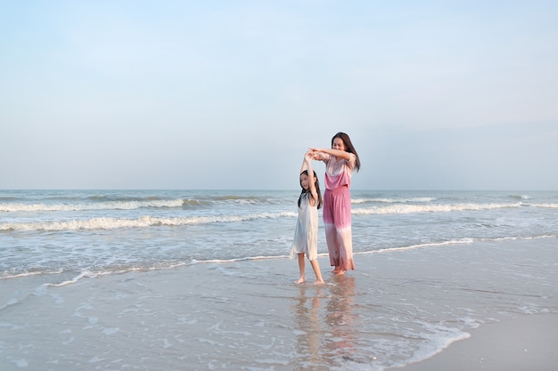 Filha e mãe asiática relaxam e dançam juntas na praia do mar nas férias.