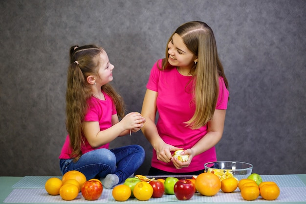 Filha e mãe cortam uma salada de frutas composta de laranja maçã e tangerina