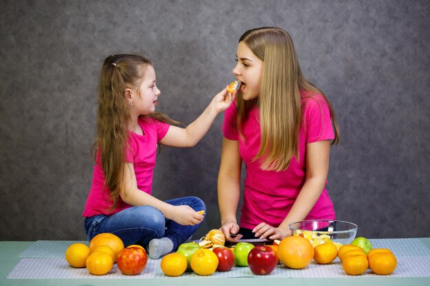 Filha e mãe cortam uma salada de frutas composta de laranja maçã e tangerina