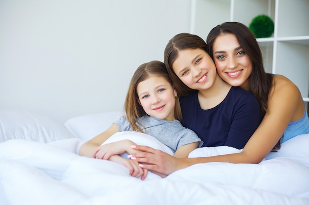 Filha e mãe linda estão abraçando, olhando e sorrindo enquanto está sentado na cama em casa