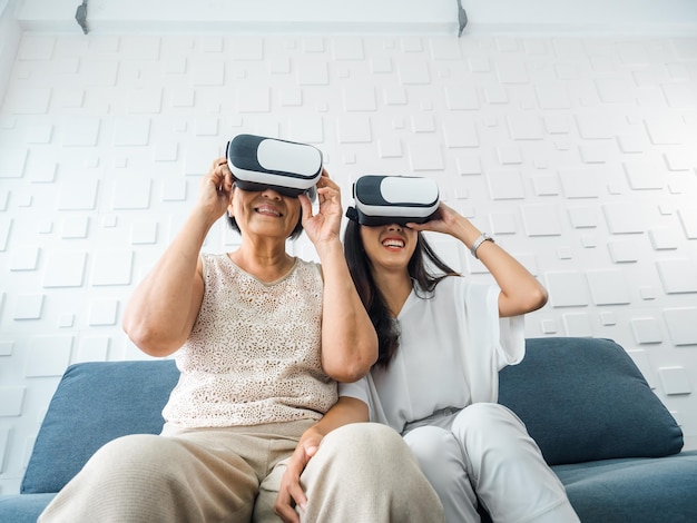 Filha feliz da jovem asiática e sua mãe idosa usando óculos VR desfrutam de jogo 3d online juntos no quarto branco Mãe e filha com conceito de estilo de vida de tecnologia virtual de realidade