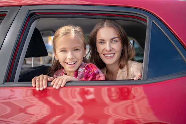 Filha feliz e mãe olhando pela janela no banco de trás do carro