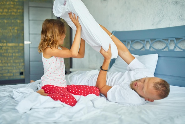 Filha feliz e pai brincando de luta de travesseiros na cama pela manhã em casa