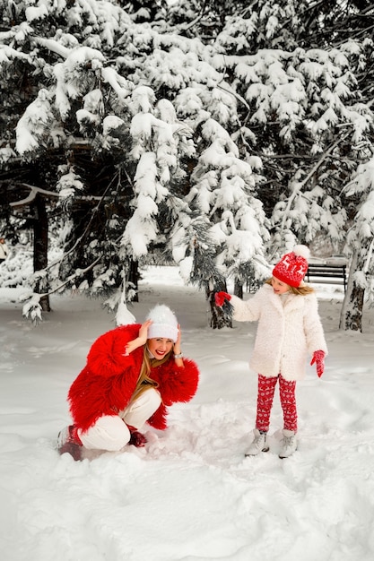 Filha joga neve de um galho de abeto na mãe. diversão de inverno. mãe e filha loira na neve