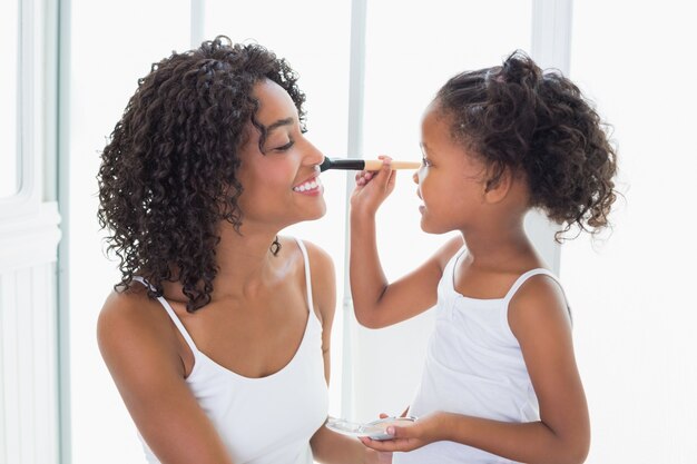 Filha linda colocando maquiagem no rosto de suas mães