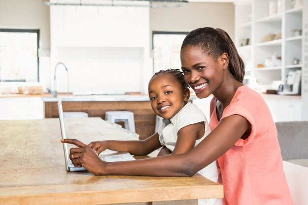 Filha linda usando laptop na mesa com a mãe