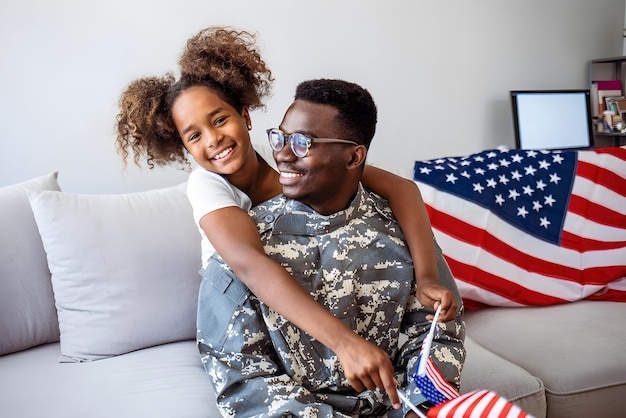 Filha menina feliz com bandeira americana abraçando o pai em uniforme militar