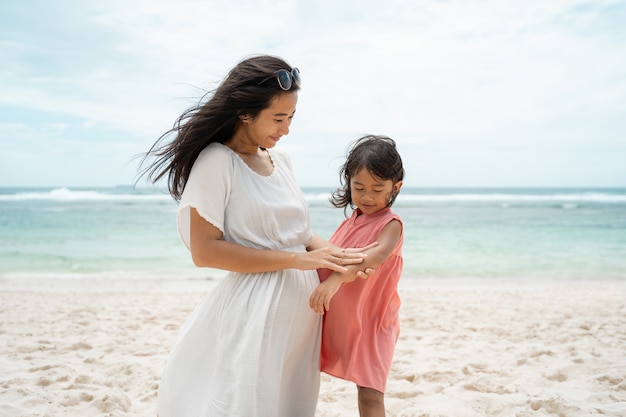 Filha olha o braço quando uma mãe esfrega protetor solar