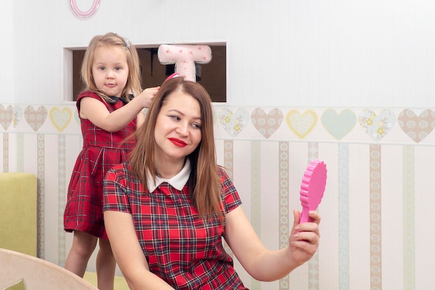 filha penteando o cabelo da mãe em pé em uma cama em um berçário