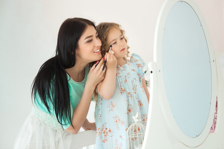 Filha pequena e sua mãe aplicando compõem um ao outro. Mãe muito jovem e adorável garota se divertindo juntos. Família fashionista bonita