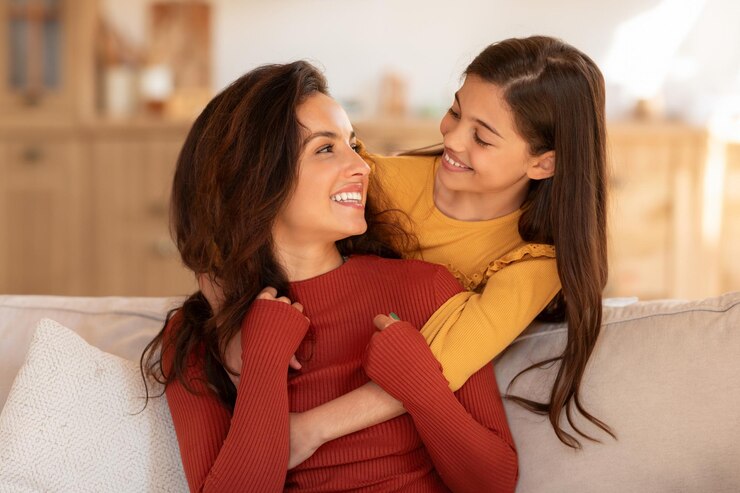 Foto filha pré-adolescente abraçando a mãe pelas costas, abraçando dentro de casa