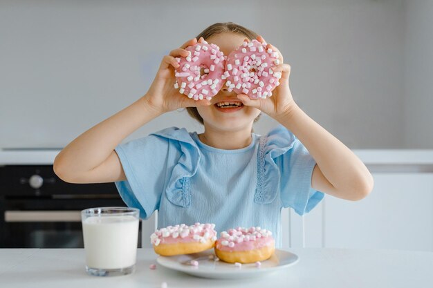 Filha se diverte com donuts coloridosEla olha pelo buraco no donut perto de seus olhos