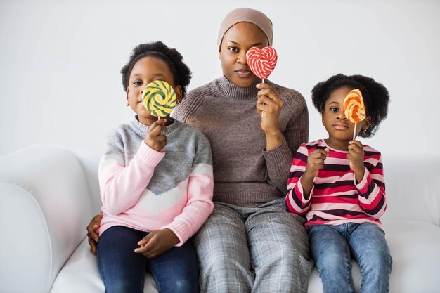 Filhas com mãe islâmica em hijab brincando com pirulitos no estúdio