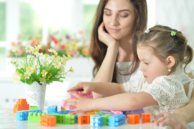 Filhinha e mãe felizes brincando com blocos de plástico coloridos em casa