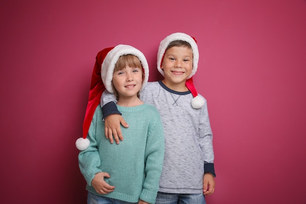 Filhinhos bonitos em chapéus de Papai Noel na superfície de cor. Conceito de natal