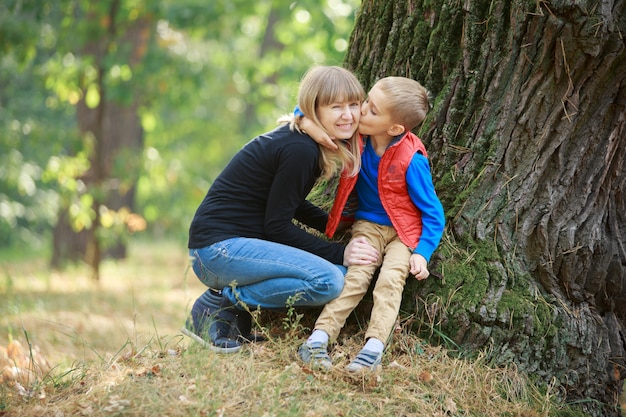 filho abraçando e beijando sua mãe grávida na natureza. menino e mulher grávida sorridente caminhando ao ar livre no parque verde. mulher grávida, aproveitando o tempo com seu filho